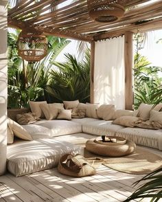 an outdoor living area with white couches and pillows on the floor, surrounded by greenery