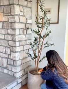 a woman sitting on the floor next to a potted plant in front of a brick wall