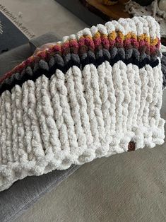 a knitted pillow sitting on top of a couch next to a pile of books