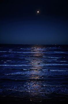 the moon is shining brightly over the ocean at night with waves coming in to shore