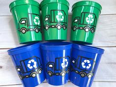 four green plastic trash cans with recycling symbols painted on the lids and sides, sitting next to each other