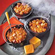 three pots of chili and cornbread on a plate