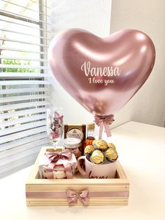 a pink heart shaped balloon sitting on top of a wooden box filled with chocolates