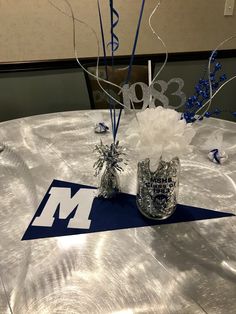 two vases with flowers are sitting on a silver table cloth covered tablecloth that is decorated with blue and white streamers