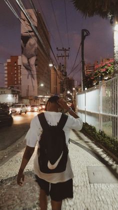 a woman walking down the street at night with her back to the camera, wearing a white shirt and black skirt