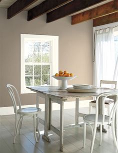 a dining room with yellow painted walls and white chairs, an oval table surrounded by fruit