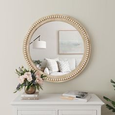 a living room with a white dresser and round mirror on the wall above it is a vase filled with flowers