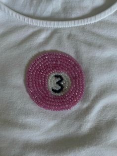 a white shirt with a pink beaded number 3 on the front and black letters on the back