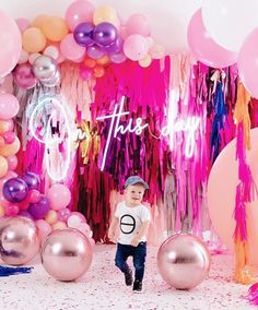 a little boy standing in front of balloons and streamers with his name on it