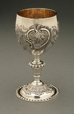 an ornately decorated silver goblet on a gray surface with a wooden lid