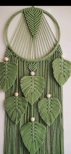 a green wall hanging with leaves and beads on the front, made out of yarn