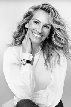 a black and white photo of a smiling woman with her hand on her chin, wearing a watch