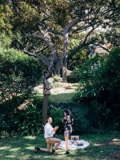 two people sitting on the ground in front of a tree and eating food from a plate