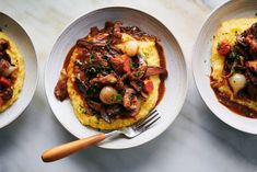 three white bowls filled with food on top of a marble counter next to a knife and fork