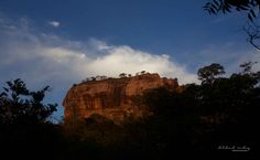 the top of a mountain with clouds in the sky and trees on the foreground