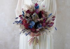 a woman in a white dress holding a bouquet of red, blue and purple flowers