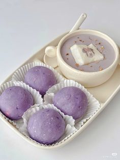 four purple desserts in paper cups on a white plate with a bowl of soup