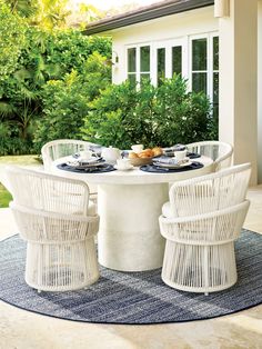 a white table with four chairs and plates on it in front of a house near some bushes