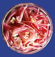 a glass bowl filled with red onions on top of a blue tablecloth next to a knife