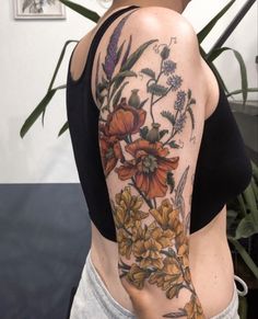 a woman with a flower tattoo on her arm and shoulder is standing in front of a potted plant