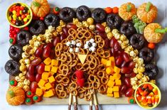 a turkey made out of pretzels, fruit and nuts on a cutting board