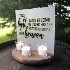 three candles sitting on top of a wooden tray next to a sign that says, this burns in honor of those who are watching today from heaven