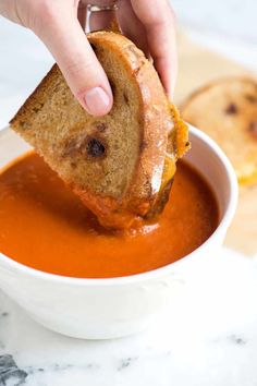 a person dipping some bread into a bowl of tomato soup