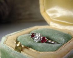 "This is a gorgeous Platinum Diamond and Ruby Ring from Circa 1960s. The center stone is genuine Oval Cut Diamond that is a \"VS\" Quality Diamond. The measurements are 5.5mm by 3.9mm making it just below a half a carat in size and an approximate size of .47 of a Carat. On each side of the center diamond are two lovely round cut genuine ruby gems. Each Ruby measures approximately 3.5mm in size which is approximately .30 in total carat weight (.15 each). This is a very pretty, petite ring with a Oval Rings With Side Stones For Anniversary, Oval Anniversary Rings With Side Stones, Diamond Ring With Side Stones For Gift, Oval Rings With Side Stones For Gift, Oval Three-stone Ruby Promise Ring, Oval Three Stone Ruby Ring For Wedding, Wedding Oval Three-stone Ruby Ring, Three Stone Ruby Ring For Anniversary, Diamond And Ruby Ring