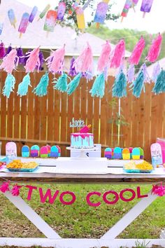 a birthday cake and decorations are on a table in front of a fence with paper streamers