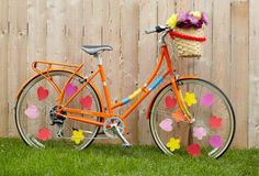 an orange bicycle with hearts painted on it parked in the grass next to a fence