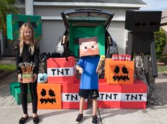 a young boy standing in front of a car with an orange and black box on it's trunk