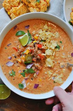 a white bowl filled with soup and topped with tortilla chips next to lime wedges