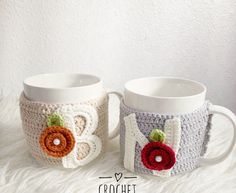 two crocheted coffee mugs sitting on top of a white furnishing