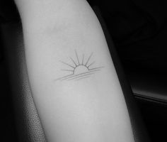 a black and white photo of a small sun tattoo on the left inner arm,