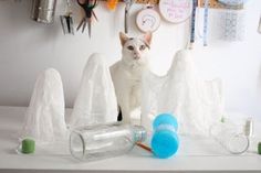 a white cat sitting on top of a table next to plastic angel wings and bottles