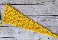 a yellow crocheted triangle next to a blue pair of scissors on a wooden surface