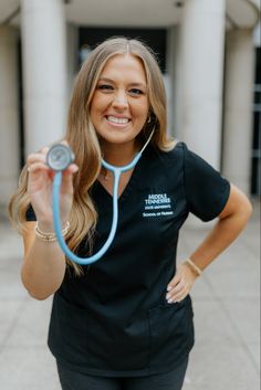 a woman with a stethoscope standing in front of a building smiling at the camera