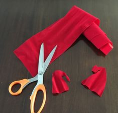 a pair of scissors sitting on top of a table next to red cloth and pieces of paper