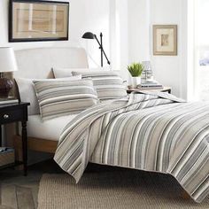 a bed with striped comforter and pillows in a room next to a lamp on a table