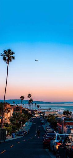 an airplane is flying over the beach and palm trees in front of houses at sunset