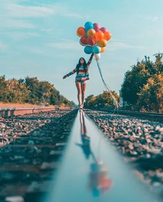 a woman is walking down the railroad tracks with balloons