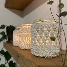 three crocheted mason jars sitting on top of a wooden shelf