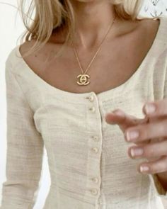 a woman in a white shirt is holding her hand out to the side and wearing a gold necklace