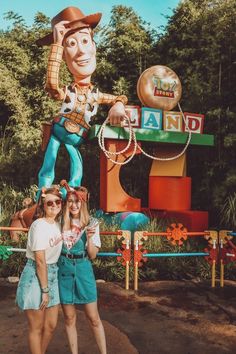 two girls standing in front of a giant toy woody the ride sign at disneyland world