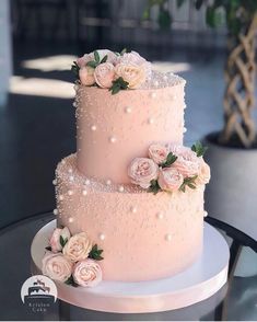 a three tiered pink wedding cake with flowers on the top and pearls on the bottom