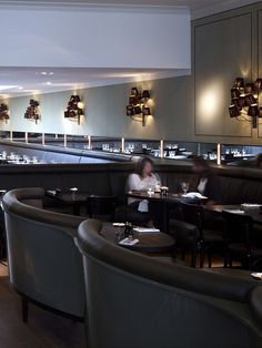 people sitting at tables in a restaurant with lights on the wall and chairs around them