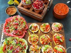 several tacos are arranged on a cutting board next to bowls of salsa and limes