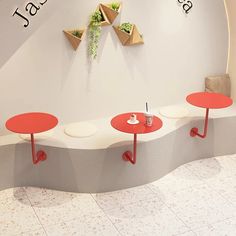 three red tables sitting next to each other in front of a white wall with plants on it