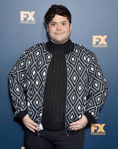 a man standing in front of a blue background wearing a black and white jacket with geometric patterns