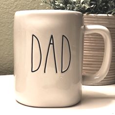 a coffee mug with the word dad written on it next to a potted plant